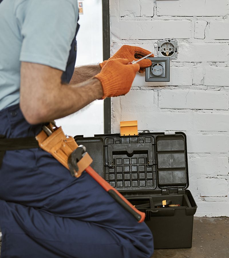 Primer plano de un técnico con guantes de trabajo usando una caja de herramientas mientras arregla el enchufe eléctrico