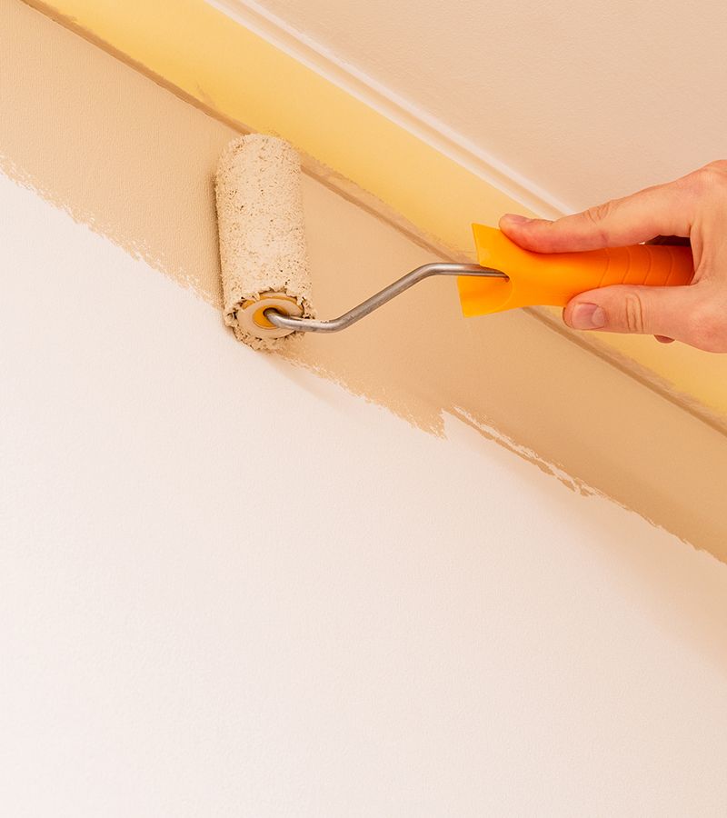 Primer plano de una mano que está pintando con un rodillo la pared en color beige.